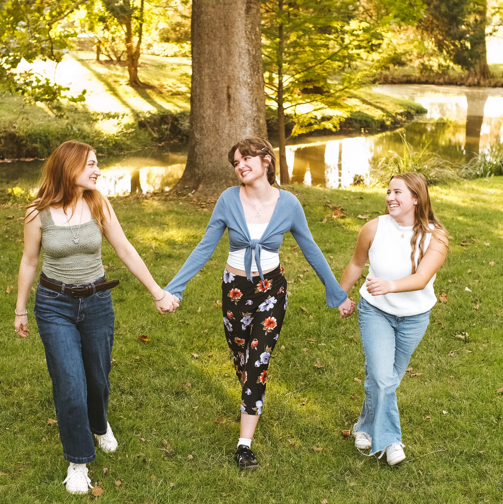 Three young women are holding hands and walking in a green field
