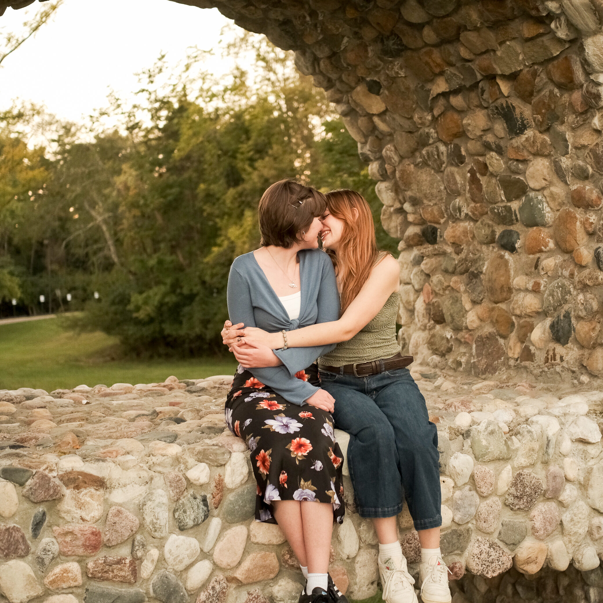 two young women are embracing and kissing while sitting in a stone archway
